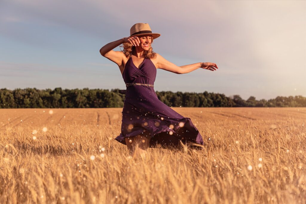 Attraktive Frau tanzt ausgelassen in einem Weizenfeld. Sie fühlt sich gesund und vital. Dank der Betreuung durch einen Health Coach ist sie wieder in ihrer hormonellen Balance und gelassen