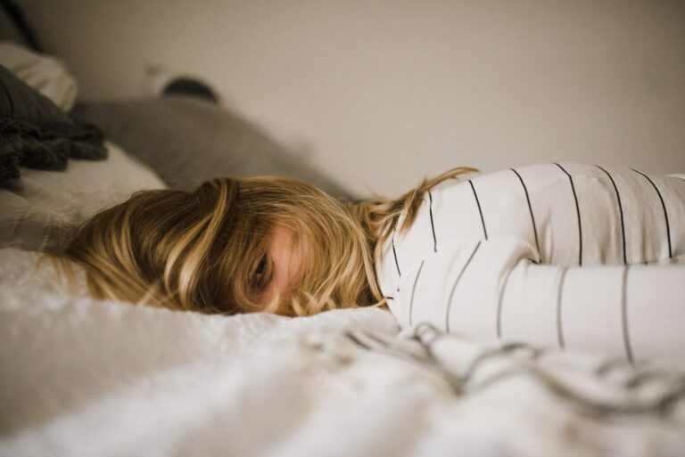 Junge Frau liegt tagsüber im Bett. Sie leidet unter Frühjahrsmüdigkeit und Erschöpfung
