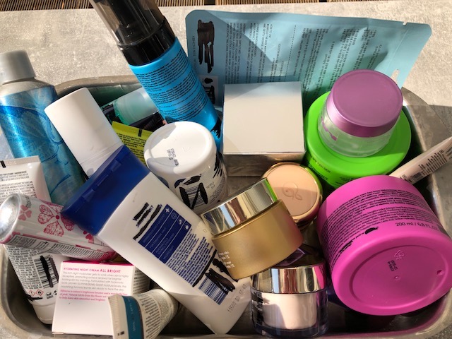 Eine Kiste voller bunter Kosmetikflaschen, Dosen und Kosmetiktiegel. Alle Gefäße sind aus Plastik. Sie enthalten Mikroplastik, was in der Kosmetik schädlich sein kann. Microplastik kann sich aus dem Plastik lösen und in die Kosmetika gelangen
