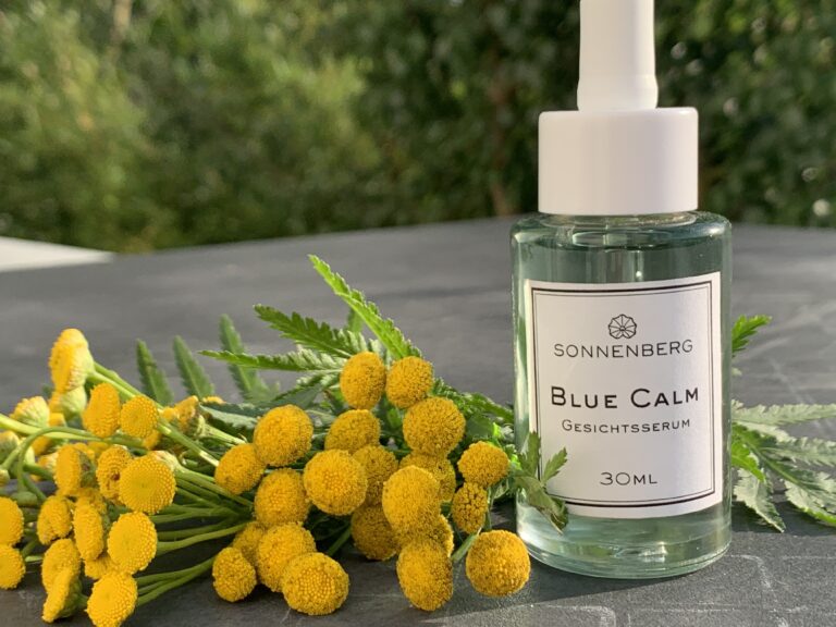 Auf dem Bild ist ein Anti-Stress Serum von Sonnenberg Skincare abgebildet. Daneben liegen die gelben Blüten des Rainfarns, aus den das blaue ätherische Öl gewonnen wird. Blue Tansy, auch blauer R ainfarn genannt, ist ein blaues Öl mit einer beruhigenden und entspannenden Wirkung in der Kosmetik. Das deep blue Öl wird gerne von Doterra oder Sonnenberg skincare verwendet