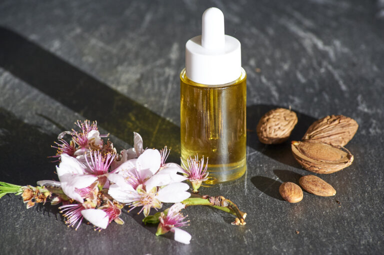 Auf dem Bild steht ein hochwertiges Gesichtsöl aus der Kategorie Wirkstoffkosmetik. Es besteht aus reinen pflanzlichen und veganen Inhaltsstoffen. Daneben liegen frische Mandeln, Mandelschalen und ein Zweig mit Mandelblüten. In dem Kosmetikprodukt ist kostbares Mandelöl enthalten. Diese und andere kosmetischen Wirkstoffe wie Distelöl, Kameliensamenöl oder Magnolien Extrakt unterstützen die Hautregeneration und schützen die Hautbarriere